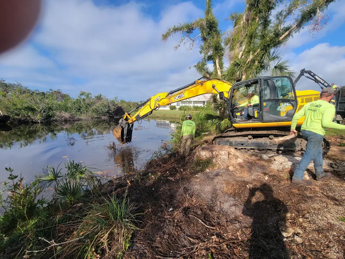 ACI crew using a tracked excavator to pull brush and debris out of a water filled canal behind a house
