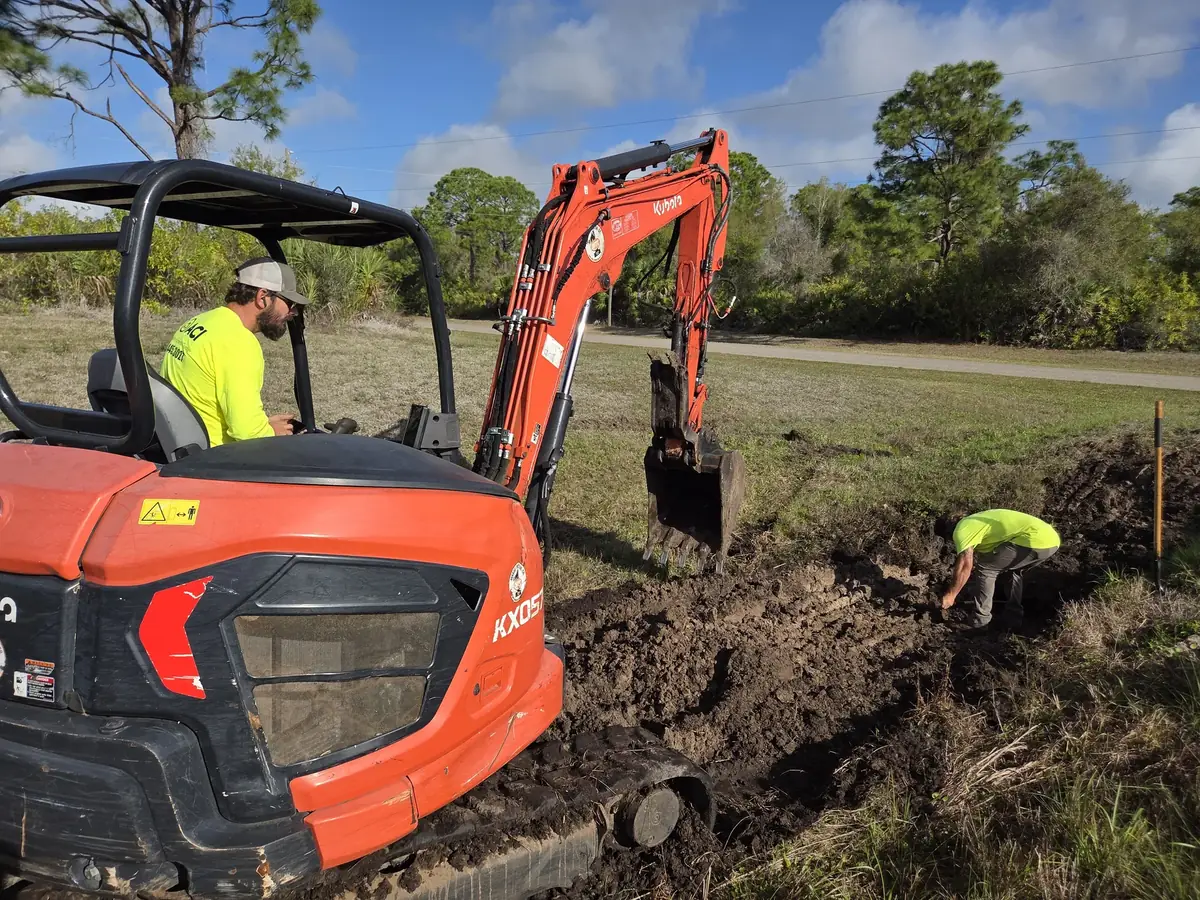 Two man crew digging out a roadside ditch with a Kubota mini excavator while one worker checks the bottom by hand