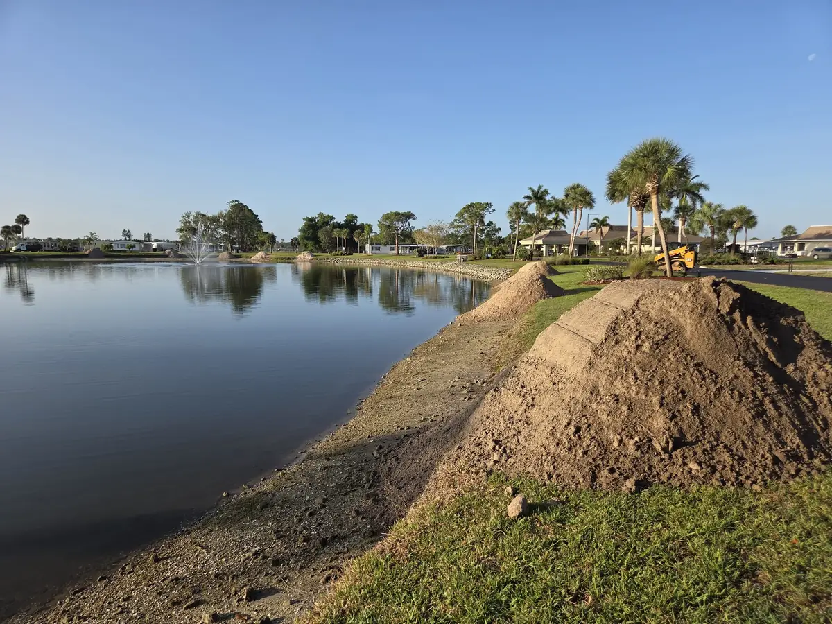 Fresh fill soil piled along a community pond bank with the fountain running behind it