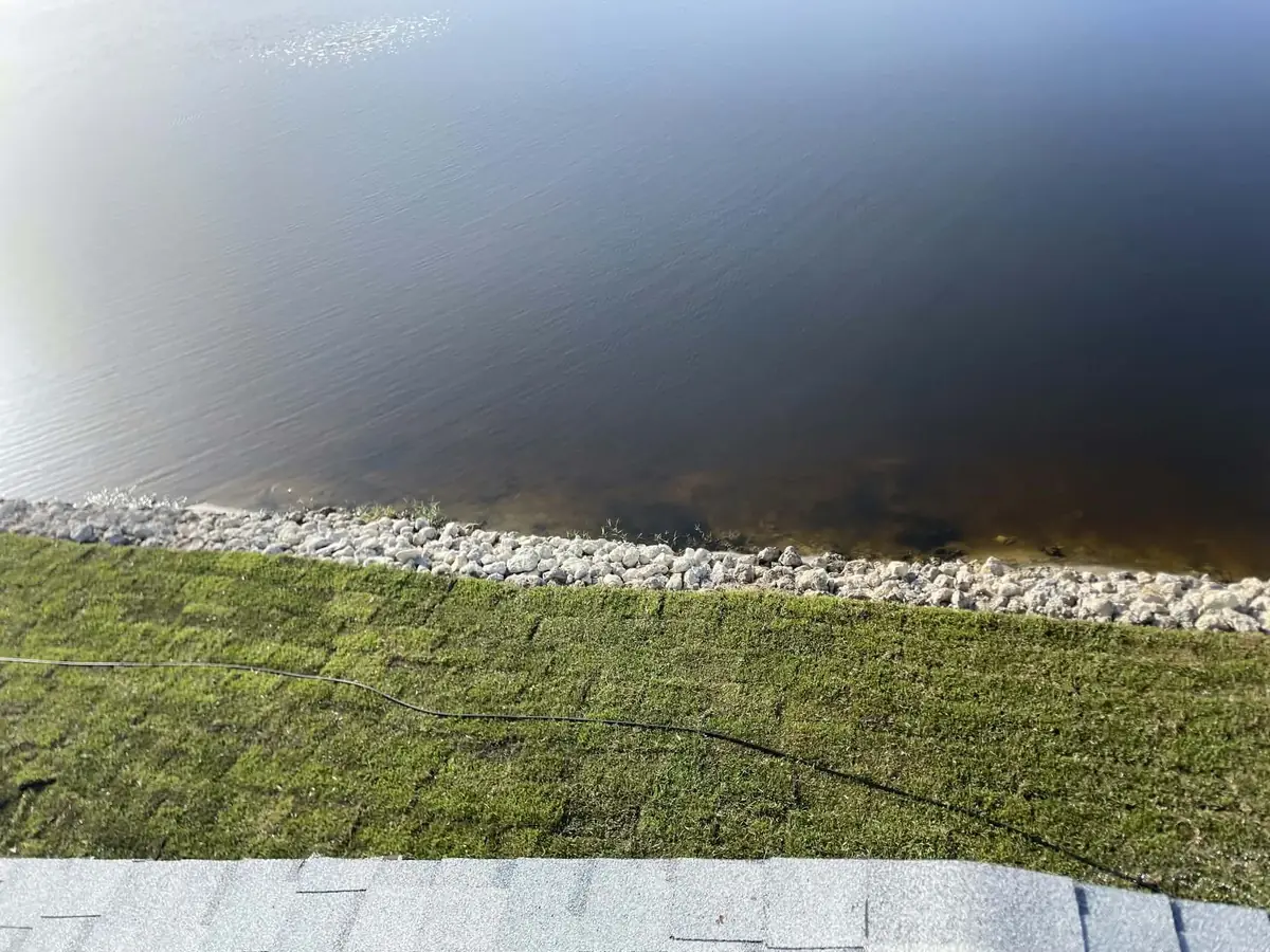 Overhead view of a lake edge with a rock band separating mowed turf from open water