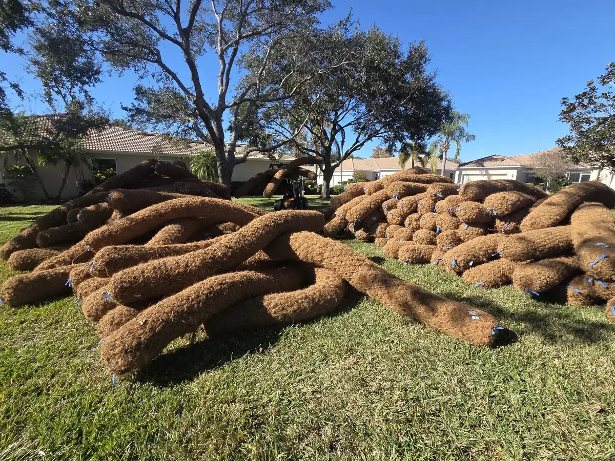 Coconut fiber logs staged on the grass before installation along the shoreline