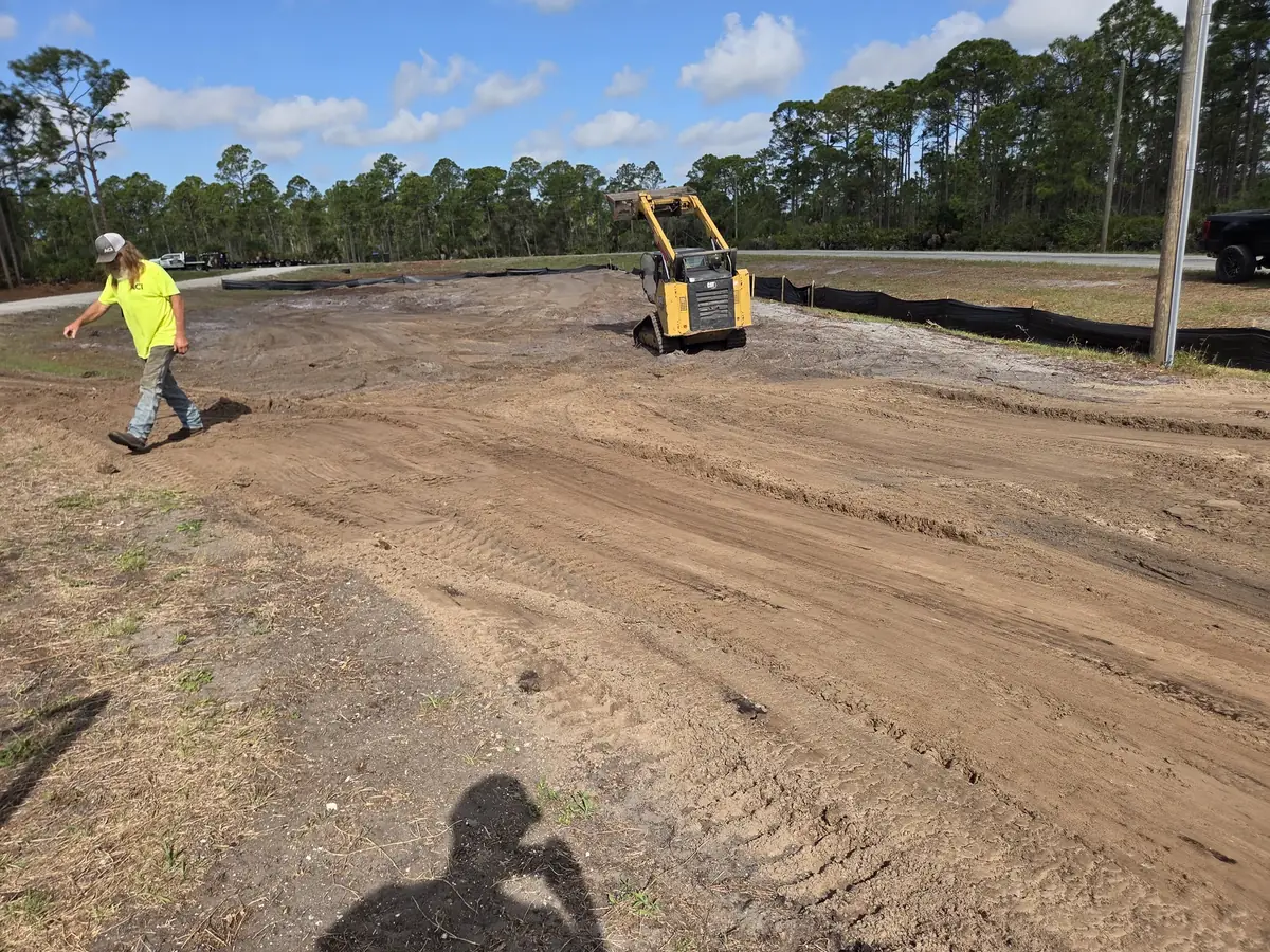 ACI crew member walking a freshly graded building lot while a tracked skid steer works behind him
