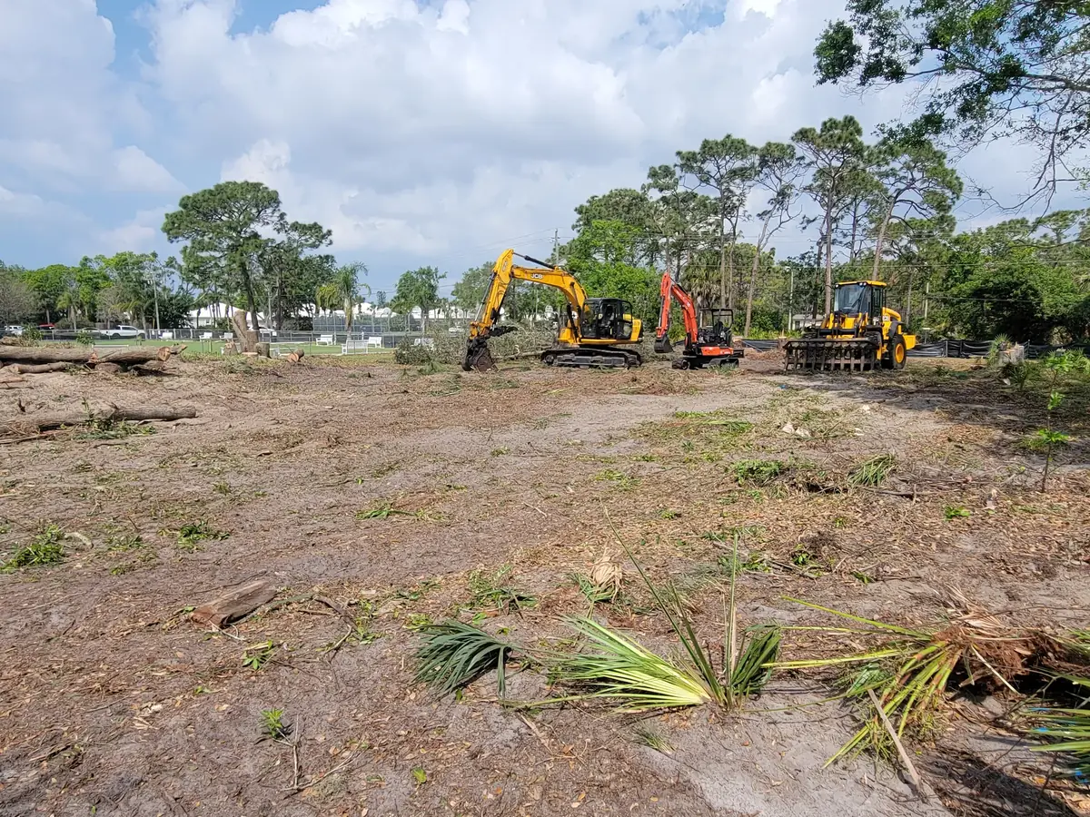 Excavator, mini excavator and a loader with a root rake parked on a lot stripped down to bare ground