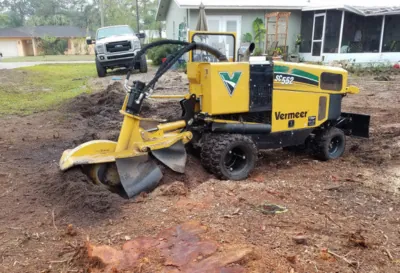 ACI operator running a diesel stump grinder into a large oak stump in a residential yard