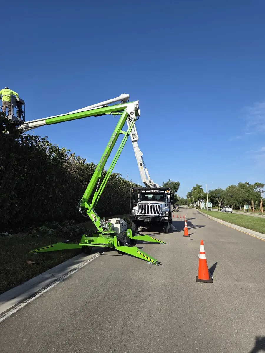 ACI crew member working from a tracked lift basket beside a bucket truck on a coned off residential street
